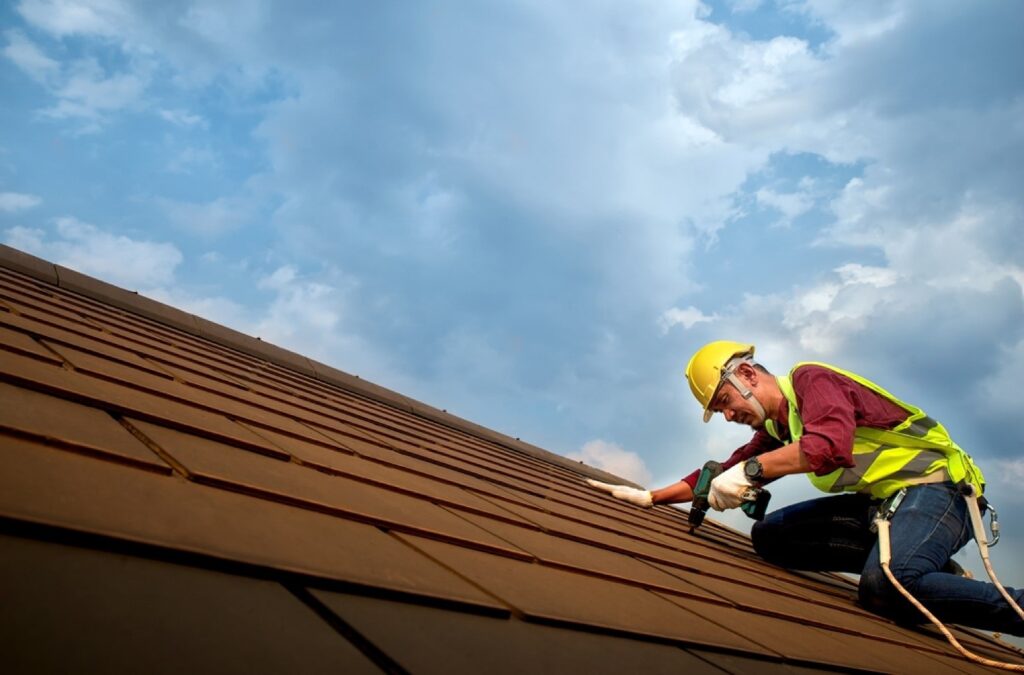 stock-photo-skilled-roof-technician-worker-working-repairing-the-roof-with-screws-drive-tools-on-the-top-of-the-1653891271-transformed-min