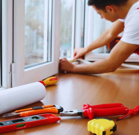 A man in red overalls is diligently repairing a window, focused on his task.