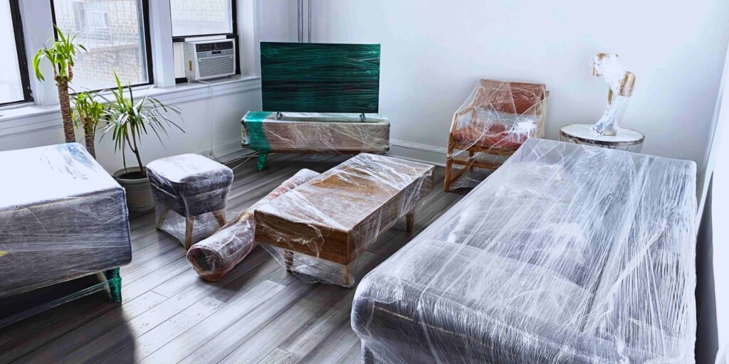 A room featuring furniture covered in plastic, indicating preparation for moving or storage.