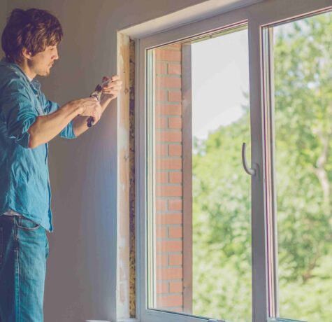 A man stands by a window, holding a plier, focused on a task.