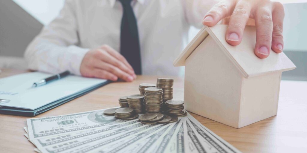 A man with house model with cash and coins.
