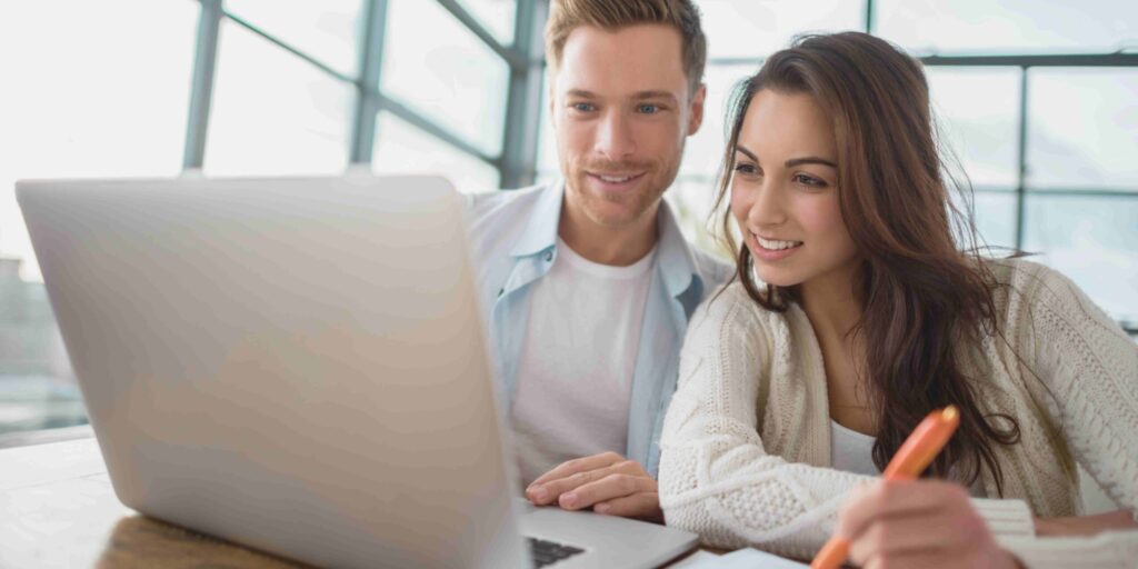 A man and woman are engaged in discussion while looking at a laptop screen together.